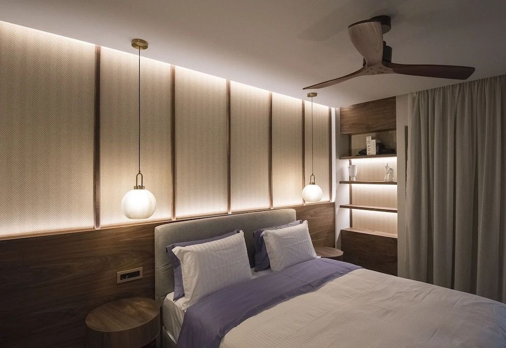 Doppelbett mit Holzkopfteil, warmem Licht, Hängeleuchten und Deckenventilator.