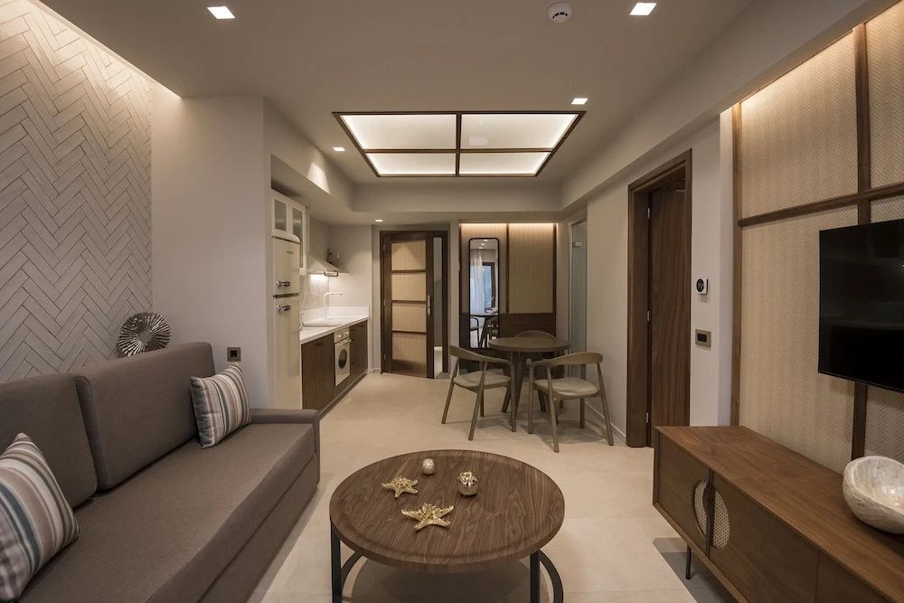 Moderner Wohnbereich einer Suite mit Sofa, Couchtisch aus Holz, Esstisch und Küchenzeile.