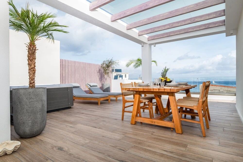 Terrasse in Holzoptik mit Esstisch, Sonnenliegen und Whirlpool mit Blick aufs Meer.