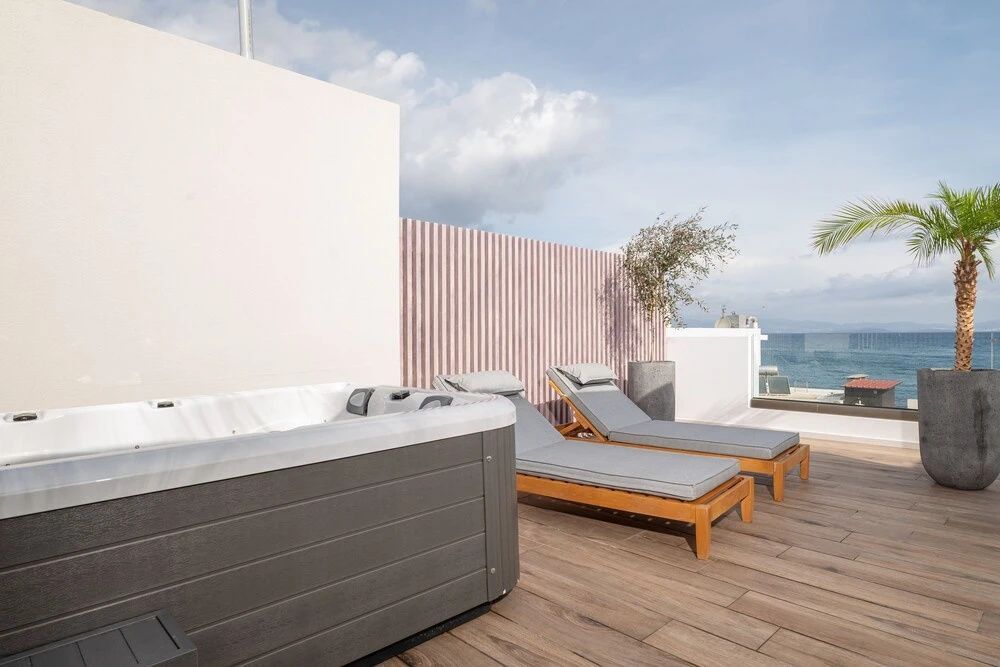 Außenwhirlpool und zwei Holzsonnenliegen auf einer Terrasse am Meer.