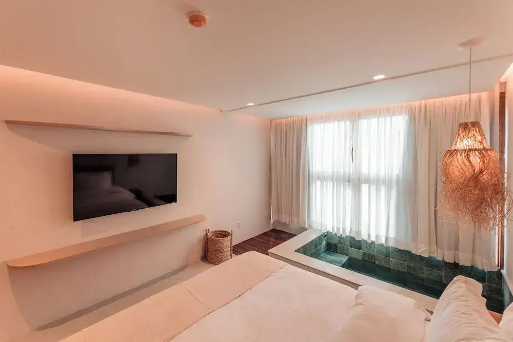 Modernes Hotelzimmer mit Bett, Wandfernseher und einem eingelassenen Whirlpool am Fenster.