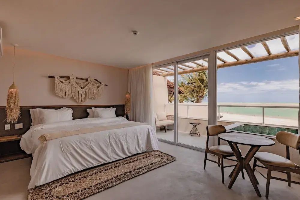 Doppelbett mit weißer Bettwäsche, Balkon mit Blick auf das Meer und Holzmöbel im Zimmer.