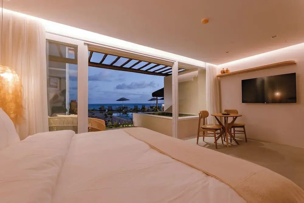 Blick aus dem Hotelzimmer auf eine Terrasse mit Whirlpool und das dahinterliegende Meer.