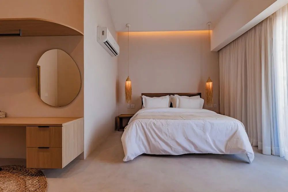 Helles Hotelzimmer mit großem Doppelbett, Holzwaschtisch und zwei Hängeleuchten.