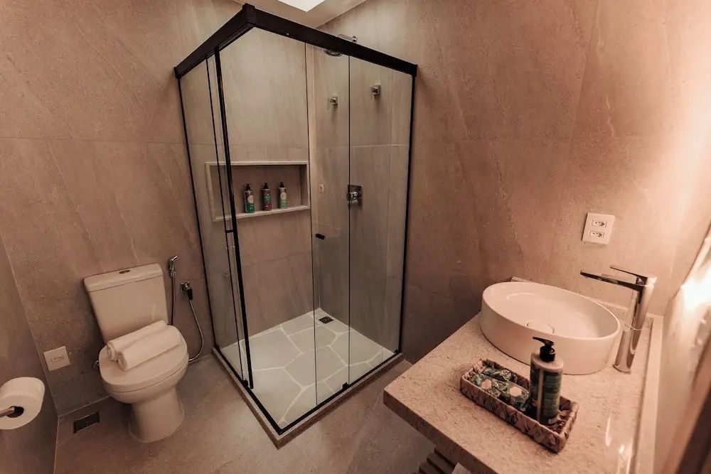Badezimmer mit einer gläsernen Duschkabine, einer Toilette und einem Waschtisch mit Pflegeprodukten.