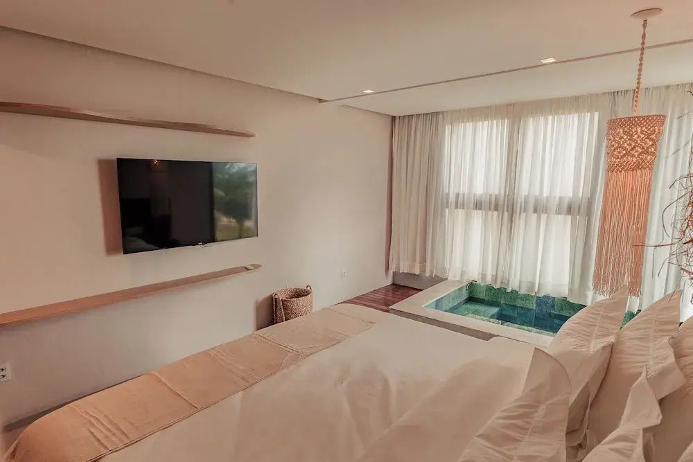 Blick vom Doppelbett auf einen Flachbildfernseher an der Wand und ein kleines Becken am Fenster.