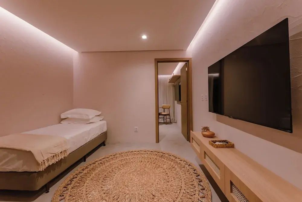 Einrichtung eines Zimmers mit Einzelbett, rundem Teppich und Fernseher an der Wand.