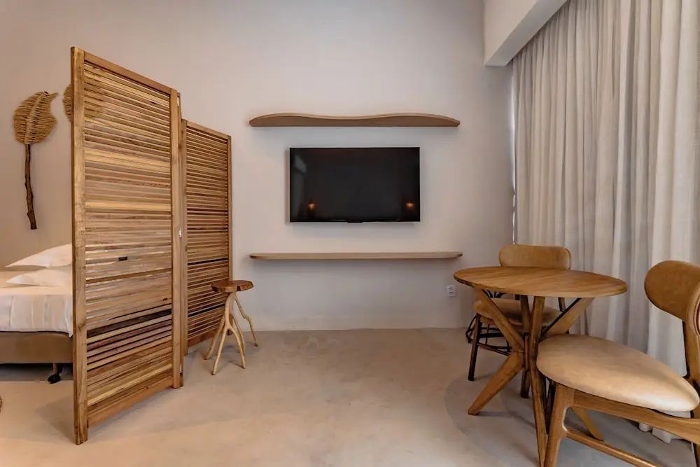 Zimmerwand mit montiertem Flachbildfernseher, Holzregalen sowie Tisch und Stühlen.