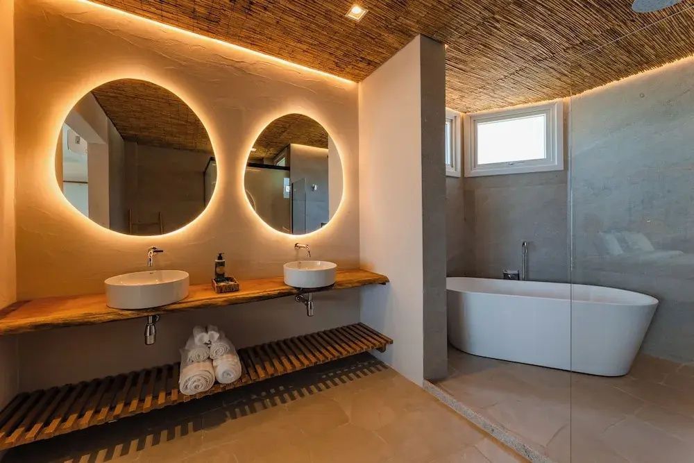 Badezimmer mit zwei Aufsatzwaschbecken, rund beleuchteten Spiegeln und Badewanne.