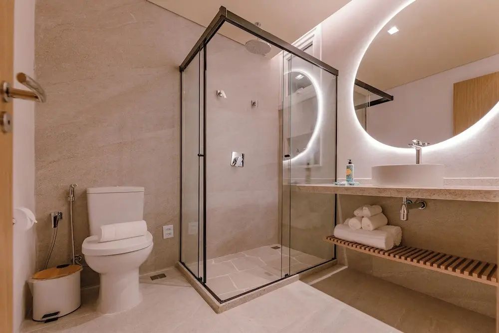 Badezimmer mit schwarz gerahmter Glasdusche, beleuchtetem Rundspiegel und Toilette.