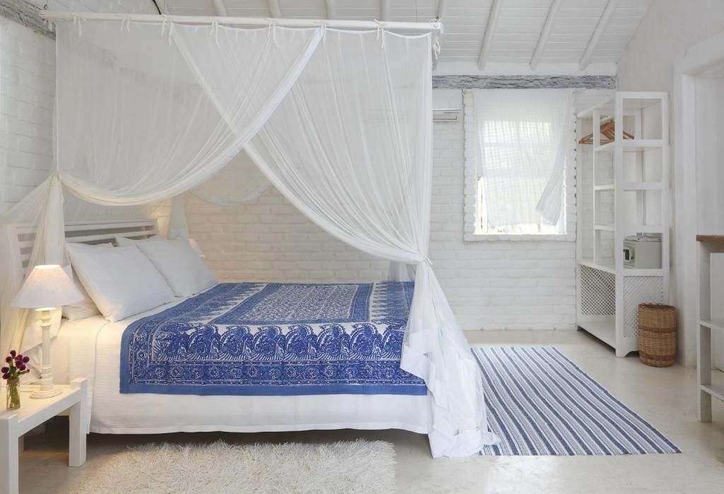 Helles Hotelzimmer mit Himmelbett, blau gemusterter Tagesdecke, Moskitonetzen und Holzfußboden.