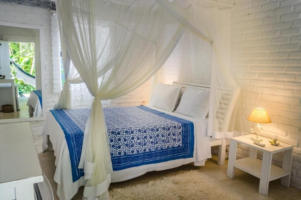 Doppelbett mit Moskitonetz und blau-weißer Tagesdecke in einem hell gestalteten Zimmer.