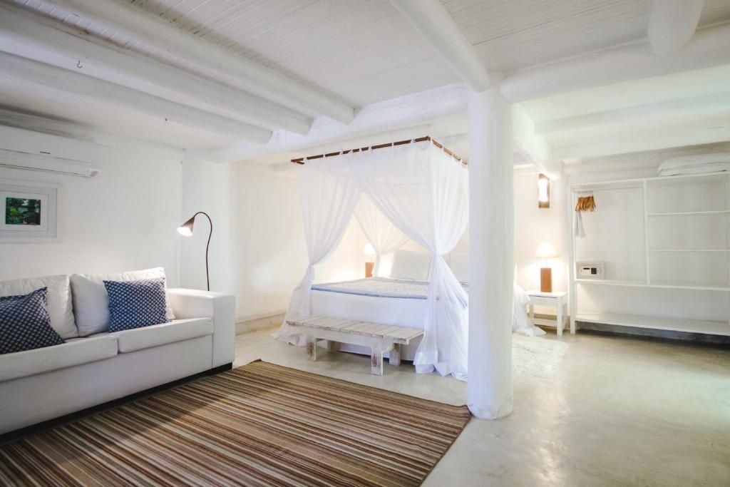 Weiß gestaltetes Hotelzimmer mit Himmelbett, Sofa und gestreiftem Teppich.