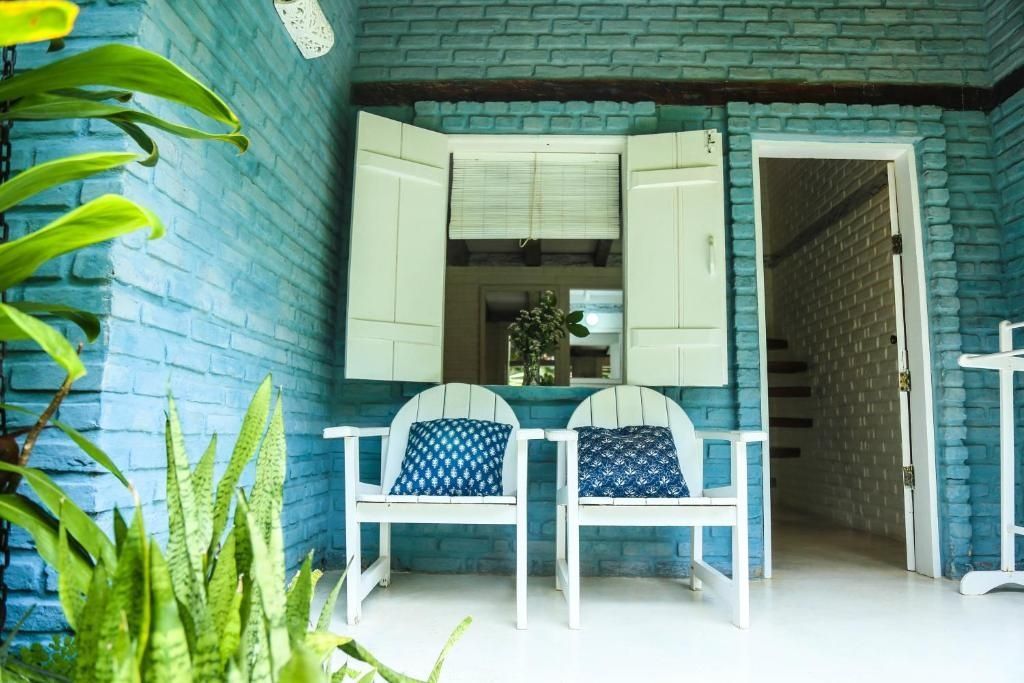 Zwei weiße Holzstühle mit gemusterten blauen Kissen auf einer blauen Veranda mit Klappläden.
