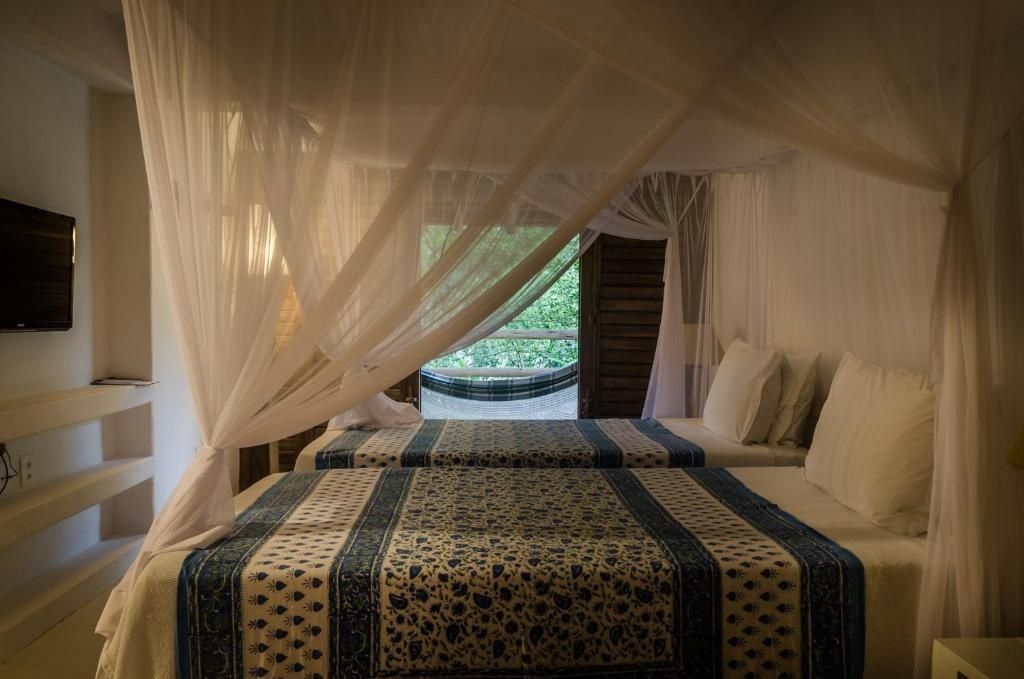 Schlafzimmer mit zwei Betten unter einem Moskitonetz und Blick auf die Hängematte.
