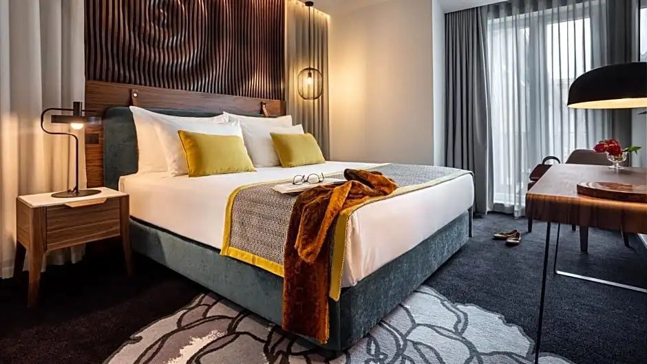 Doppelbett mit gelben Kissen, Wurfdecke und gemustertem Teppich im Hotelzimmer.