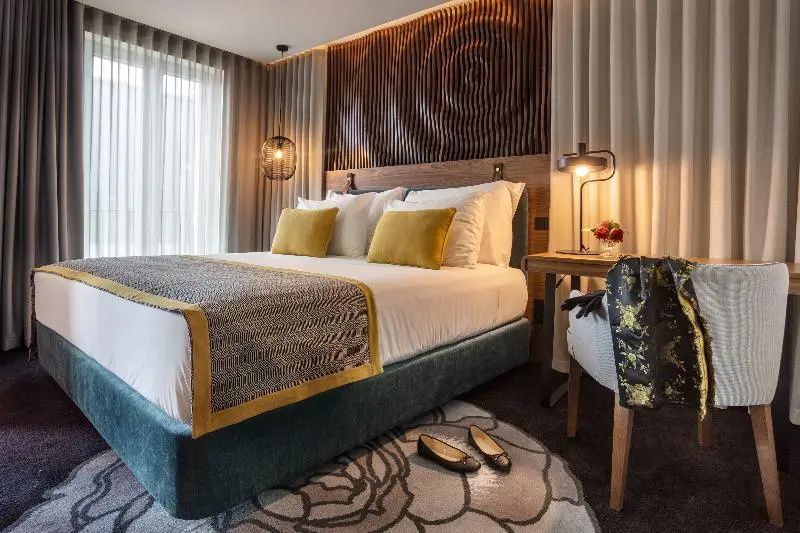 Doppelbett mit gelben Kissen, Holzkopfteil und Teppich mit Blumenmuster im Hotelzimmer.