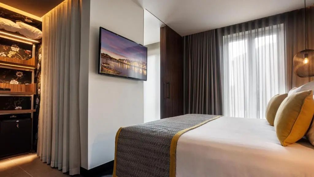 Bettfußende und Flachbildfernseher an einer weißen Wand im modernen Hotelzimmer.