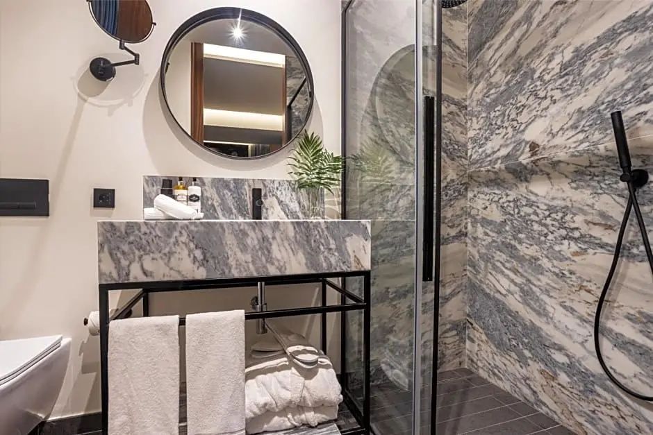 Modernes Badezimmer mit Waschtisch aus marmoriertem Naturstein, rundem Spiegel und Dusche.
