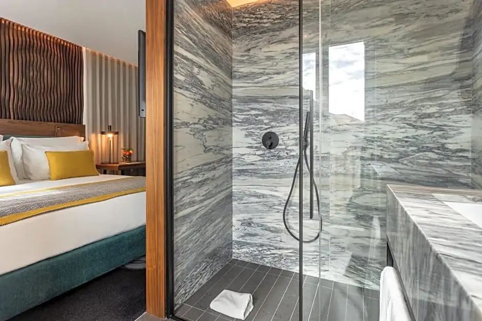 Dusche mit grauer Marmorwand und Glastür neben dem angrenzenden Schlafbereich.