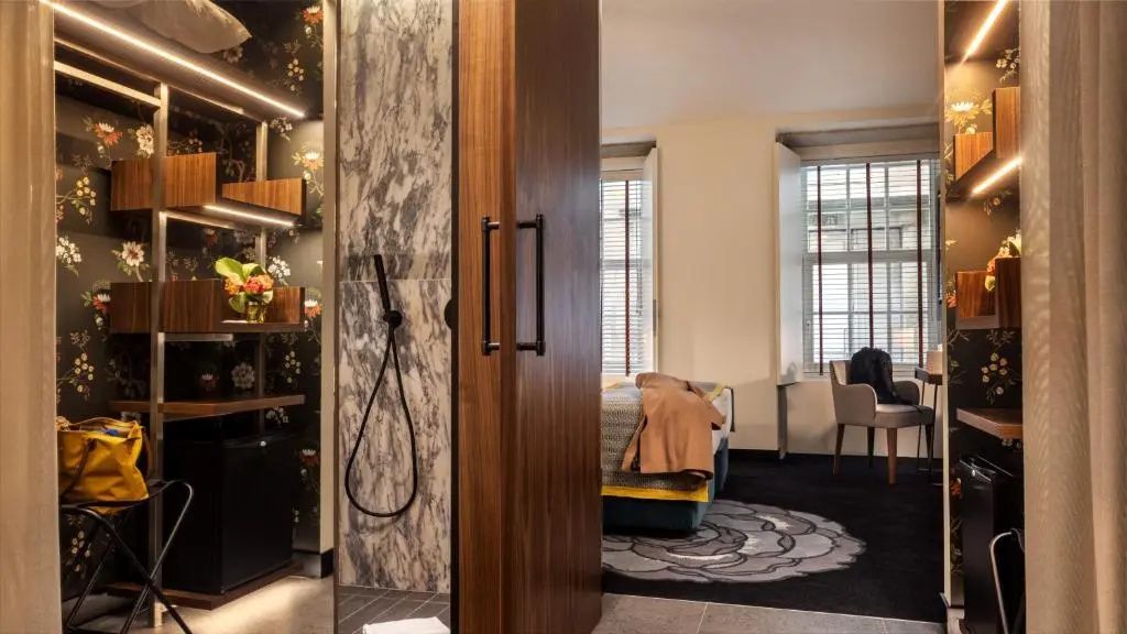Blick auf eine moderne Dusche mit Marmorwand und schwarzer Armatur neben dem Schlafbereich.