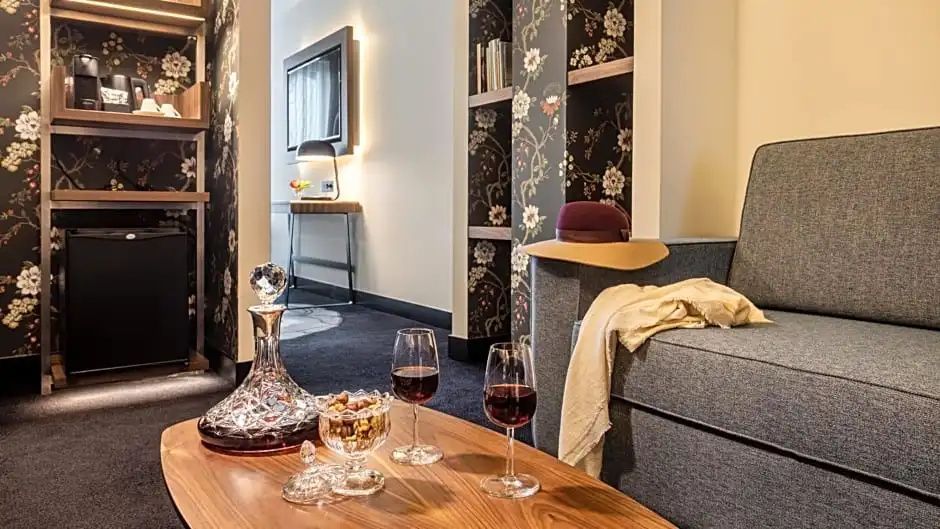 Holztisch mit Weingläsern, Karaffe und Snacks neben einem Sofa im Hotelzimmer.