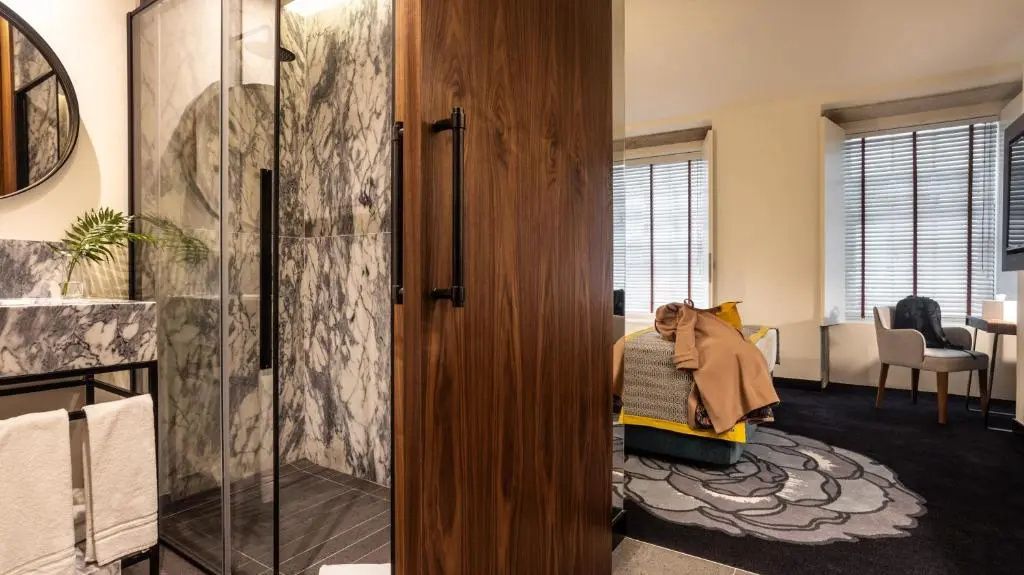 Transparente Duschkabine aus Glas mit Marmorwand und einer Holztür zum Zimmer.