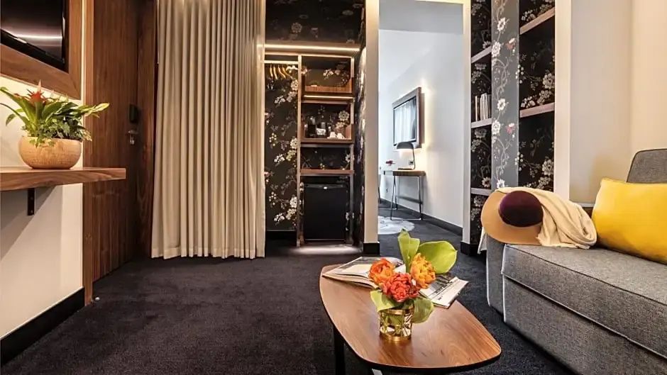 Wohnbereich einer Suite mit Couchtisch, Blumen, Vorhängen und Minibar Schrank.