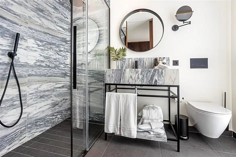 Badezimmer mit Dusche aus Marmor, Waschtisch auf Metallgestell und rundem Wandspiegel.
