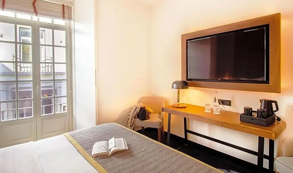 Blick auf das Bett mit aufgeschlagenem Buch und einen Schreibtisch mit Fernseher.