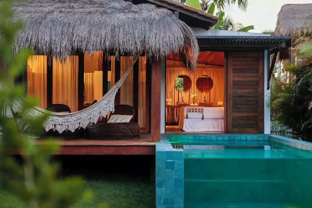 Terrasse eines Bungalows mit Hängematte, beleuchtetem Privatpool und Blick ins Zimmer.