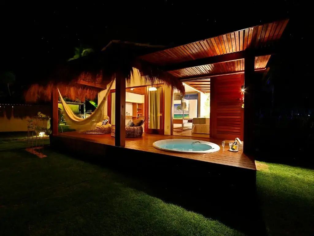 Beleuchtete Holzterrasse eines Bungalows bei Nacht mit Whirlpool und Hängematte.