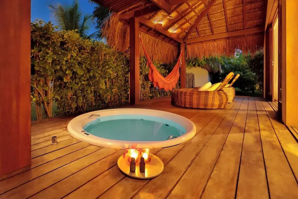 Runder Whirlpool auf einer Holzterrasse unter einem Reetdach bei Abendbeleuchtung.