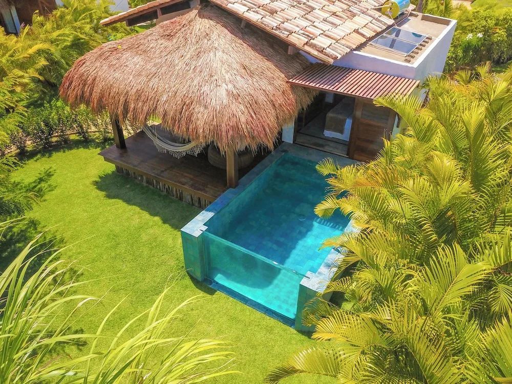 Reetgedeckter Bungalow mit privatem Swimmingpool aus Glas und Hängematte im Garten.
