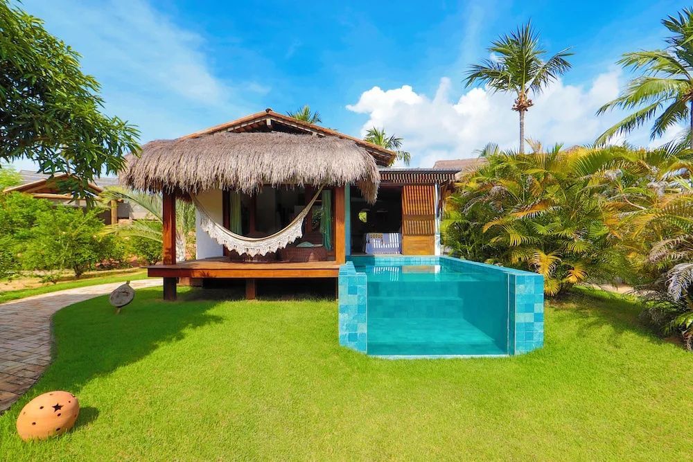 Bungalow mit Reetdach, überdachtem Freisitz, Hängematte und gläsernem Privatpool.