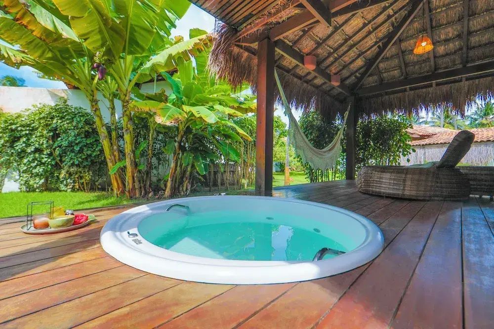 Runder Whirlpool auf einer Holzterrasse neben einer überdachten Veranda mit Hängematte im Garten.