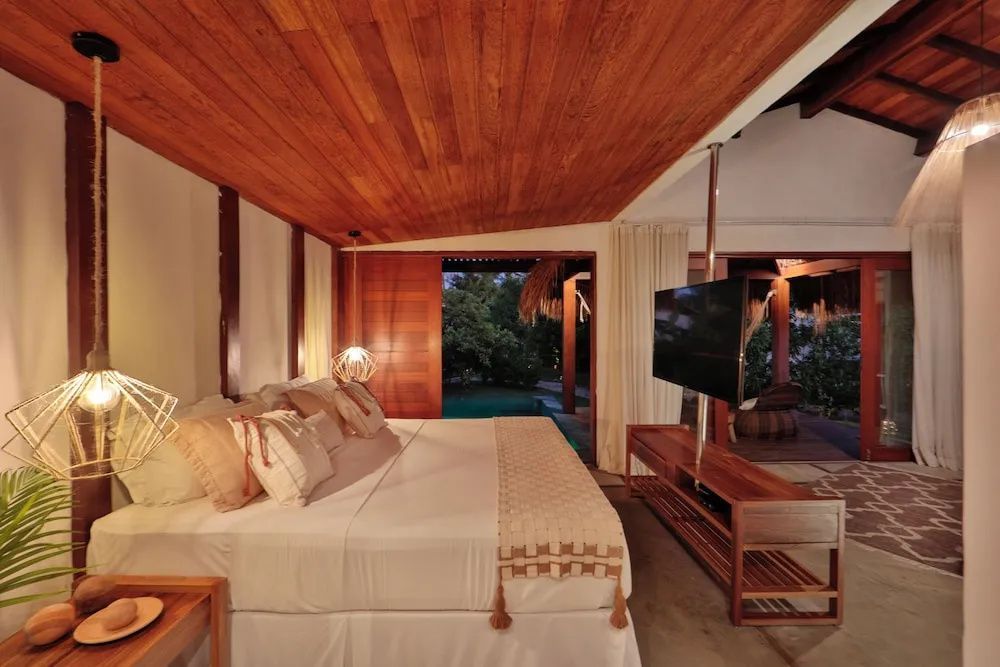 Schlafzimmer mit großem Doppelbett, Holzdecke, Fernseher und Blick ins Grüne.