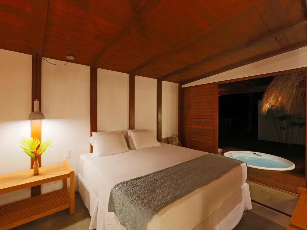 Doppelbett in einem Zimmer mit Holzdecke und Zugang zu einer Terrasse mit Whirlpool.