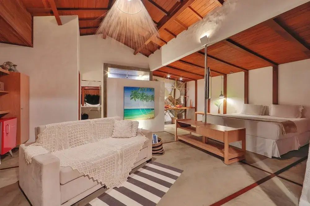 Offener Wohnbereich einer Suite mit hellem Sofa, gestreiftem Teppich und Holzdecke.