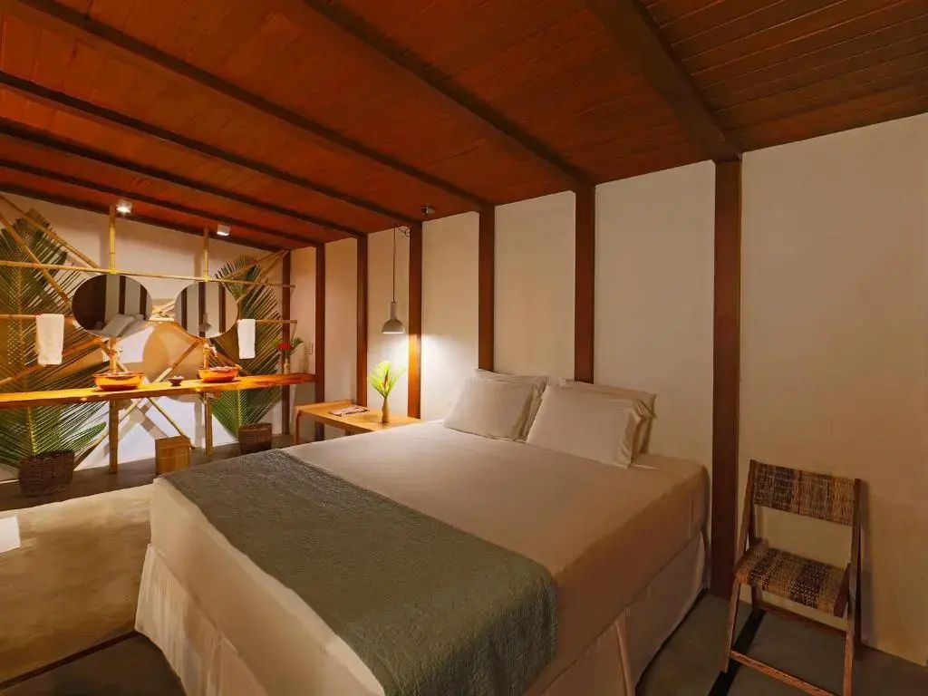 Doppelbett unter einer Decke aus Holz mit offenem Badezimmerbereich im Hintergrund.