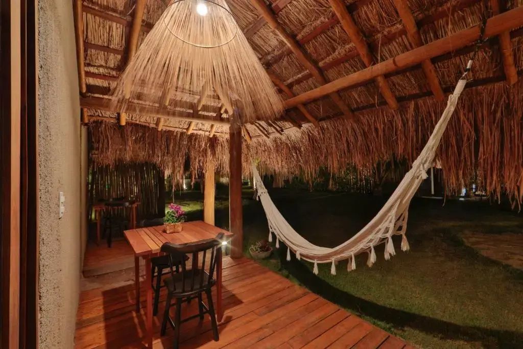 Überdachte Terrasse mit Holzmöbeln, Hängematte und einer gewebten Lampe bei Nacht.