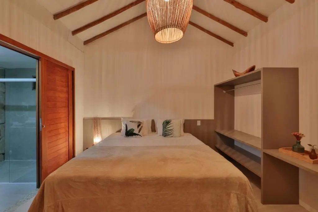 Hell eingerichtetes Zimmer mit Doppelbett, Holzgebälk am Dach und geflochtener Deckenleuchte.