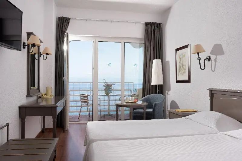 Doppelzimmer mit weißer Bettwäsche, Sessel und Balkon mit Meerblick.