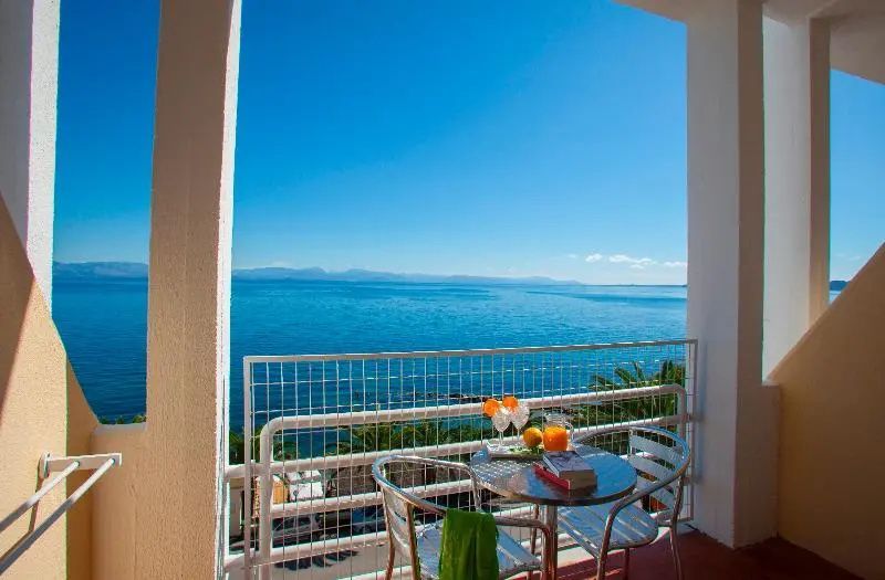 Blick vom Balkon mit Sitzgelegenheiten auf das weite blaue Meer und die Küste.