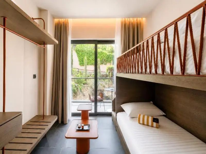 Modernes Familienzimmer mit Stockbett, kleinem Tisch und Blick ins Grüne.