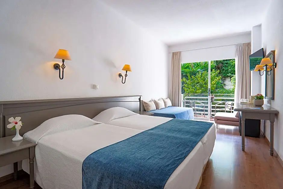 Doppelbett im Hotelzimmer mit blauem Überwurf und Zugang zum Balkon.