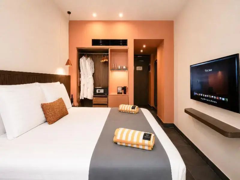 Doppelbett mit grauer Tagesdecke, offener Kleiderschrank und Flachbild-TV an der Wand.