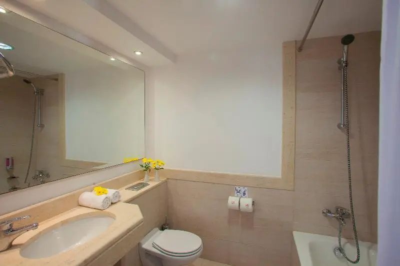 Badezimmer mit beige gefliesten Wänden, großem Spiegel, Waschtisch und Toilette.