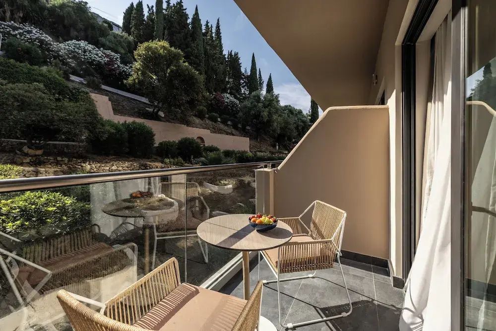 Balkon mit zwei Stühlen, einem kleinen Tisch und Blick auf eine grüne Hügellandschaft.