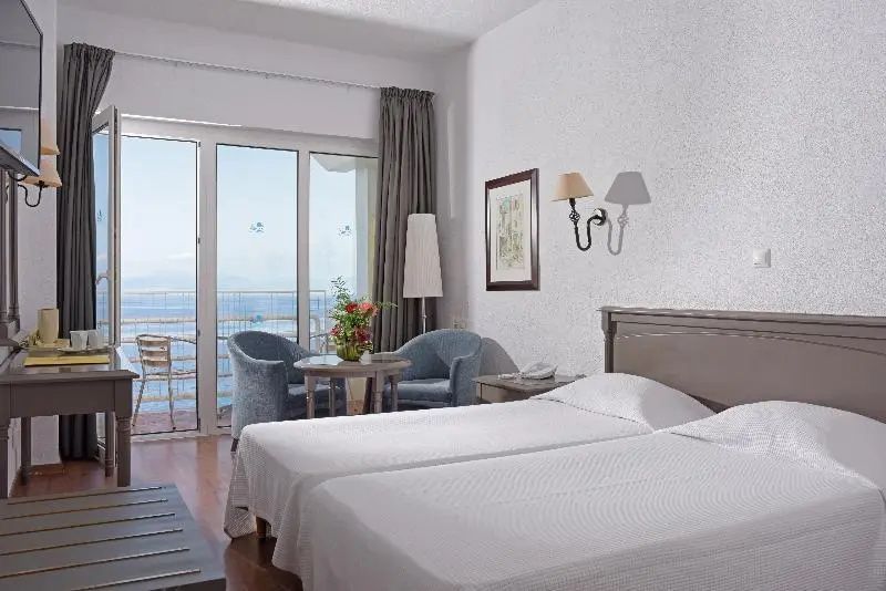 Bett im Doppelzimmer mit Sitzbereich und Glastür zum Balkon.